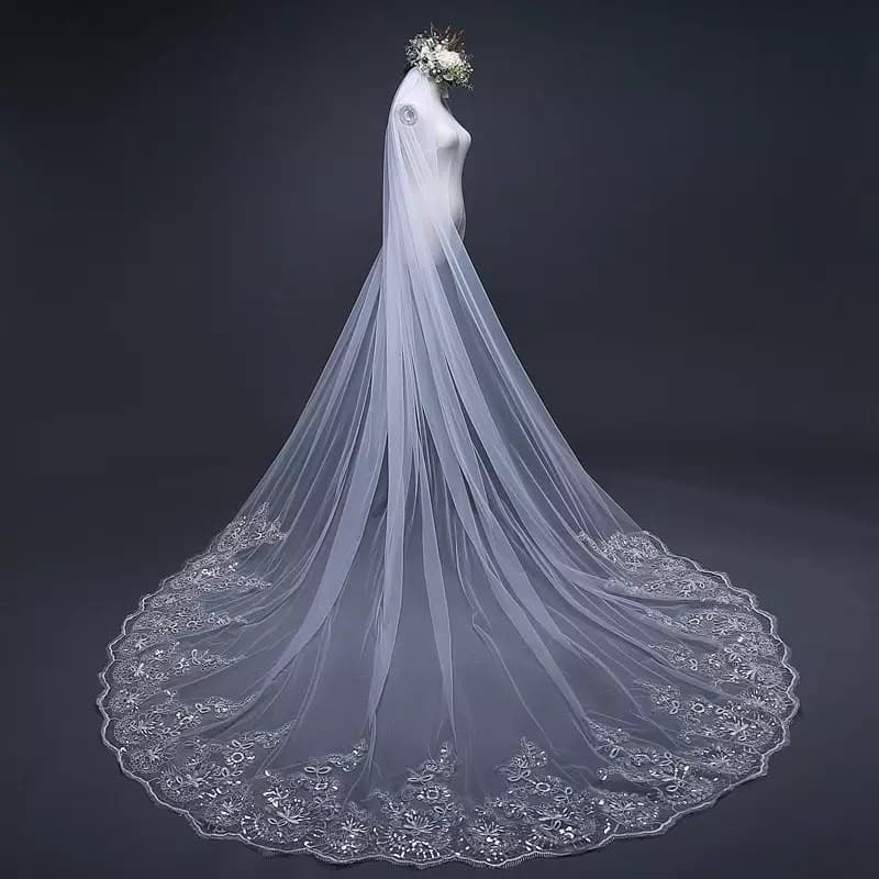 A cathedral-length veil edged in scalloped floral lace, spread out behind a dress form