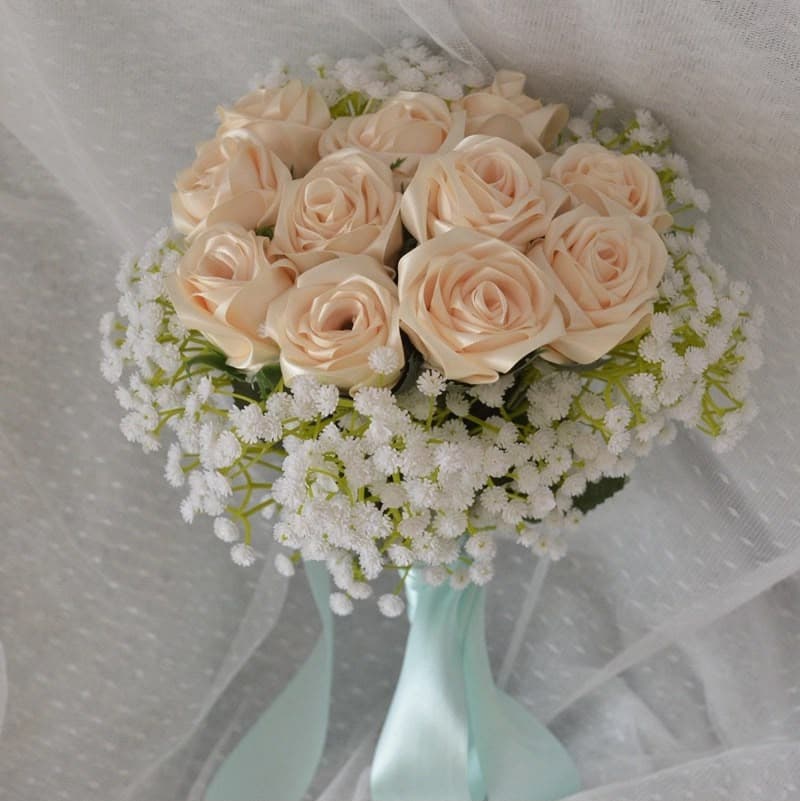 A bridal bouquet of champagne satin roses and gypsophila, bound with mint ribbon