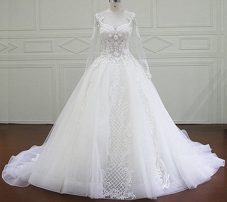 A white ball gown with long lace sleeves and an embroidered front panel, on a mannequin